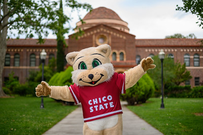 Chico State mascot Willie Wildcat stands with arms open wide in front of Kendall Hall.