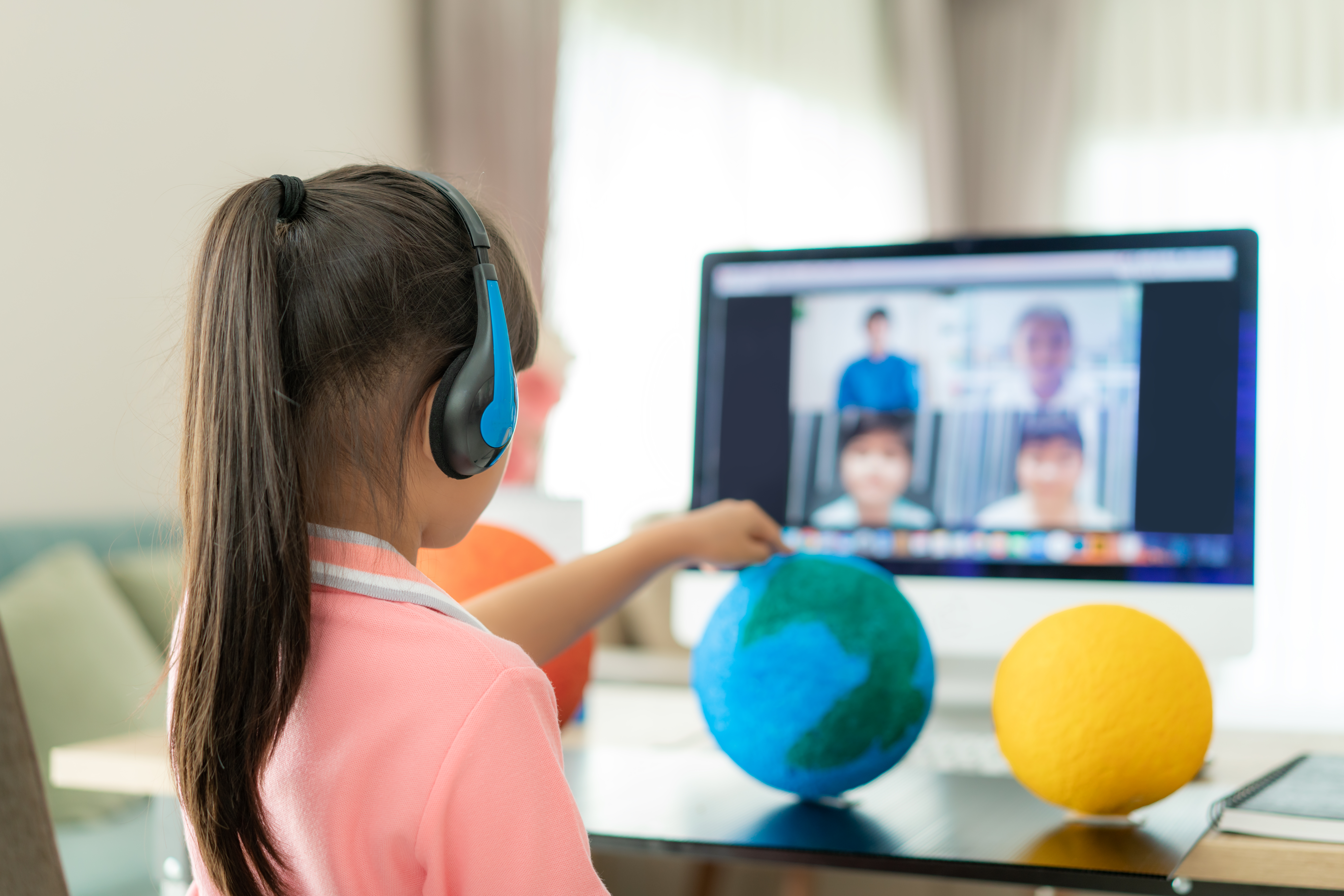 Young student learns about the planetary system online with their peers. Student is pointing to the earth with a headset on, talking to class, digitally. Distance Education at its finest. 