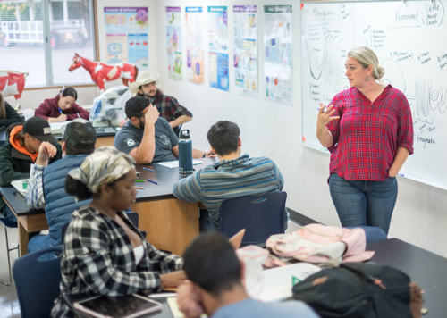 Teacher in a classroom talking to a group of students. 