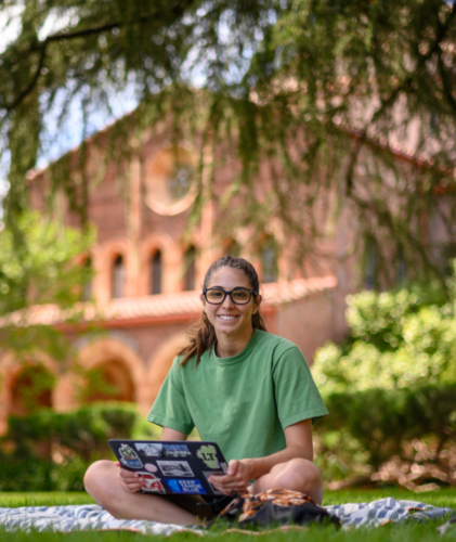 Chico State student sits with laptop in front of Kendall Hall.